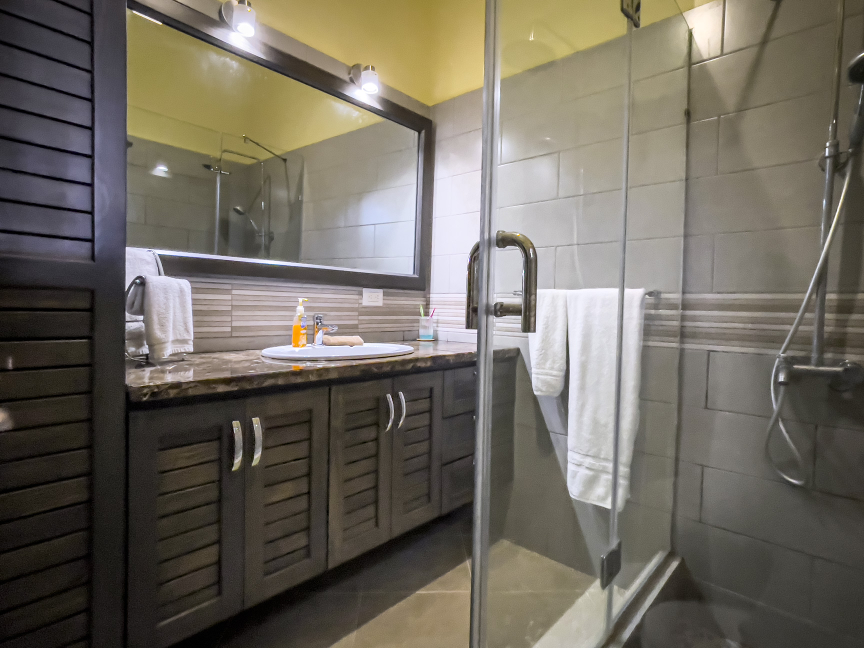 buyDRproperty Bathroom in a stunning 2 bedroom villa. Dark wood vanity, glass shower, and white towels. Sosua Real Estate