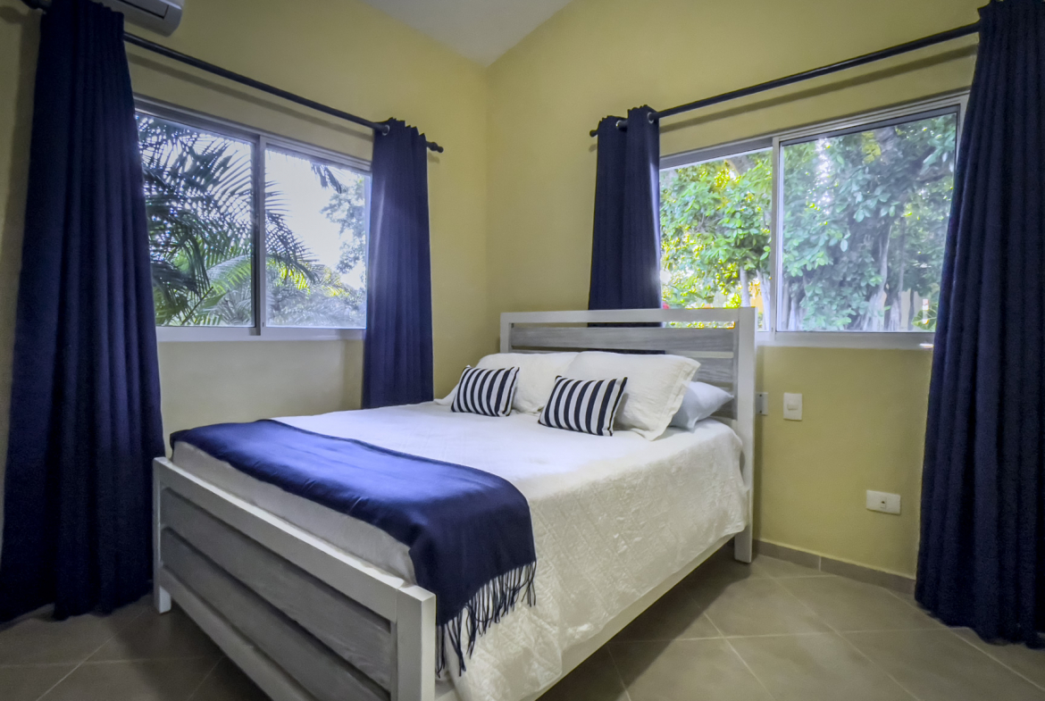 buyDRproperty Bedroom in a Stunning 2 Bedroom Villa with blue curtains and a white bed. Sosua Real Estate