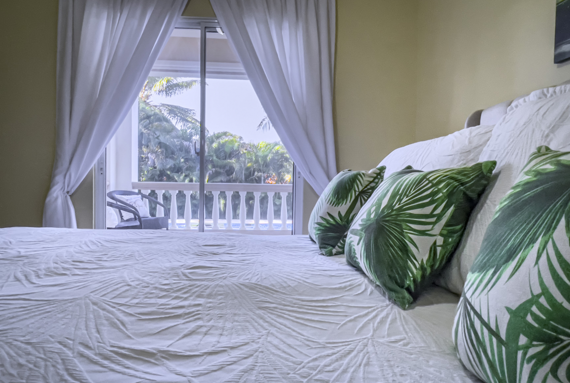 buyDRproperty Bedroom of a stunning 2 bedroom villa with white bedding and green palm pillows, overlooking a tropical view. Sosua Real Estate