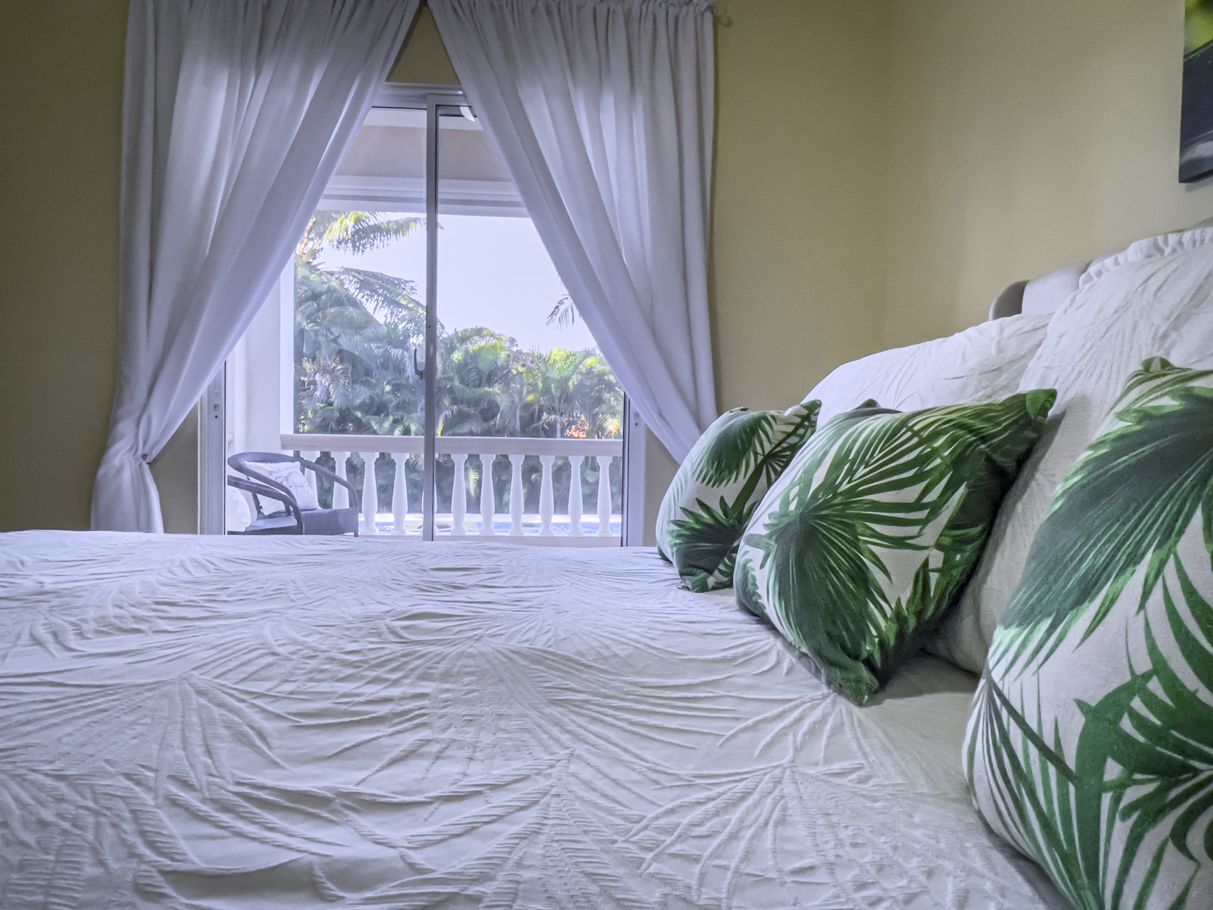 buyDRproperty Bedroom of a stunning 2 bedroom villa with white bedding and green palm pillows, overlooking a tropical view. Sosua Real Estate