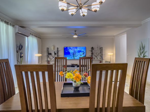 buyDRproperty Dining room of a 3 Bedroom Oceanfront Condo with wooden table and chairs, flowers, and a TV. Sosua Real Estate