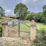 buyDRproperty Gated entrance to building lot with stone pillars, lush landscaping, and thatched roof building. Sosua Real Estate