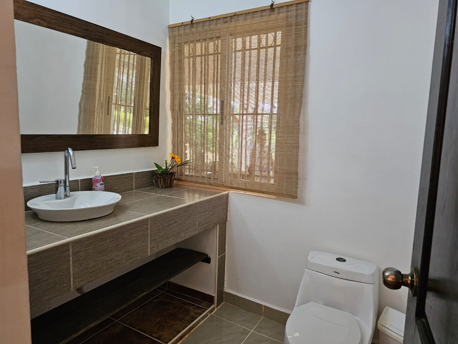 buyDRproperty Bathroom with a modern sink, mirror, woven window shade, and toilet in a Sosua villa. Sosua Real Estate