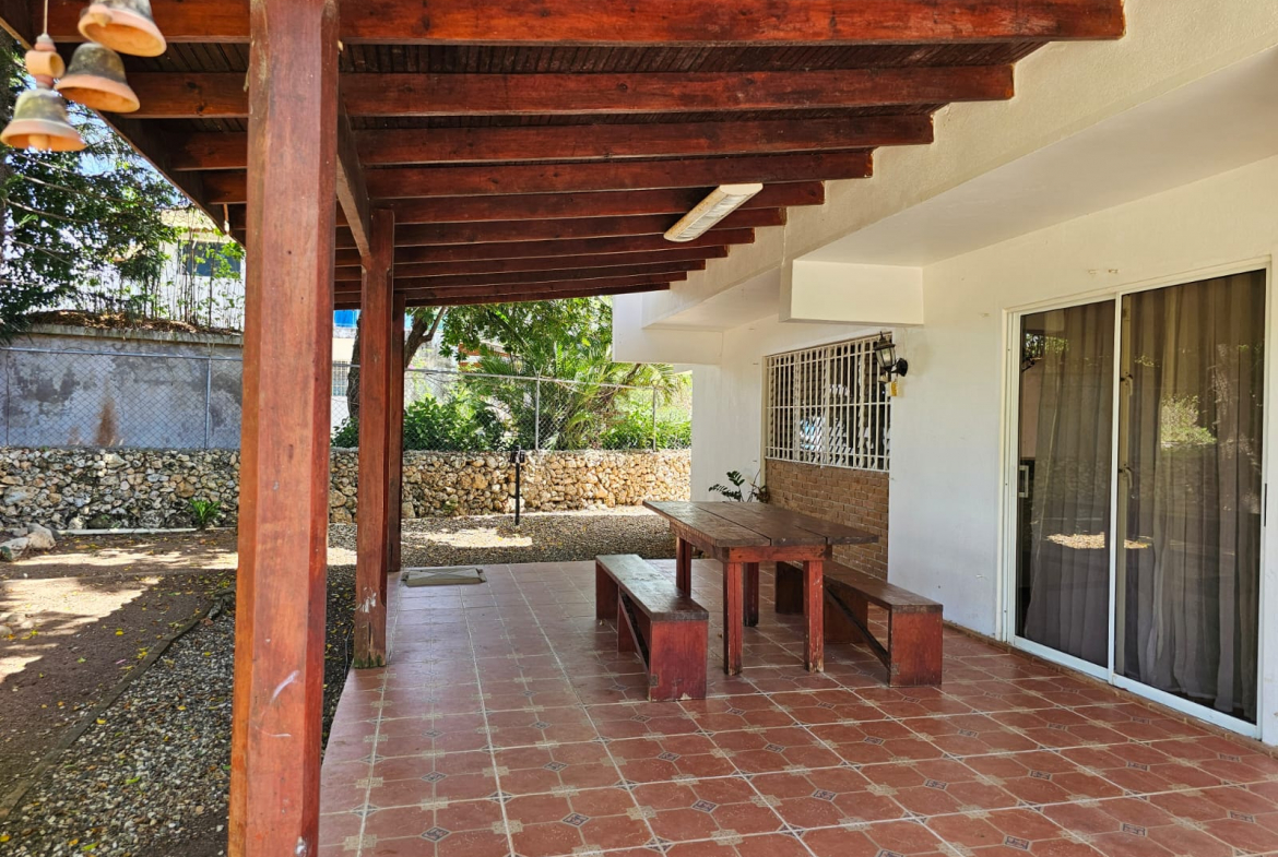 buyDRproperty Covered patio with wooden table and benches at this unique Sosua villa, tiled floor, and garden views. Sosua Real Estate