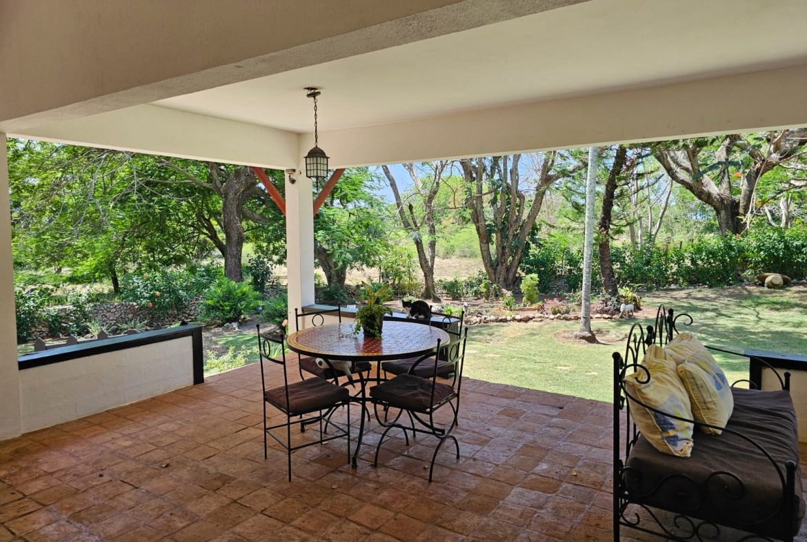 buyDRproperty Covered patio with dining set and daybed overlooking a lush garden at this unique Sosua villa. Sosua Real Estate