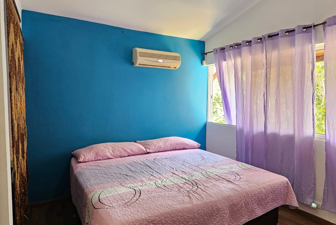 buyDRproperty Bedroom with blue accent wall, pink bedding, and purple curtains in a unique Sosua villa. Sosua Real Estate