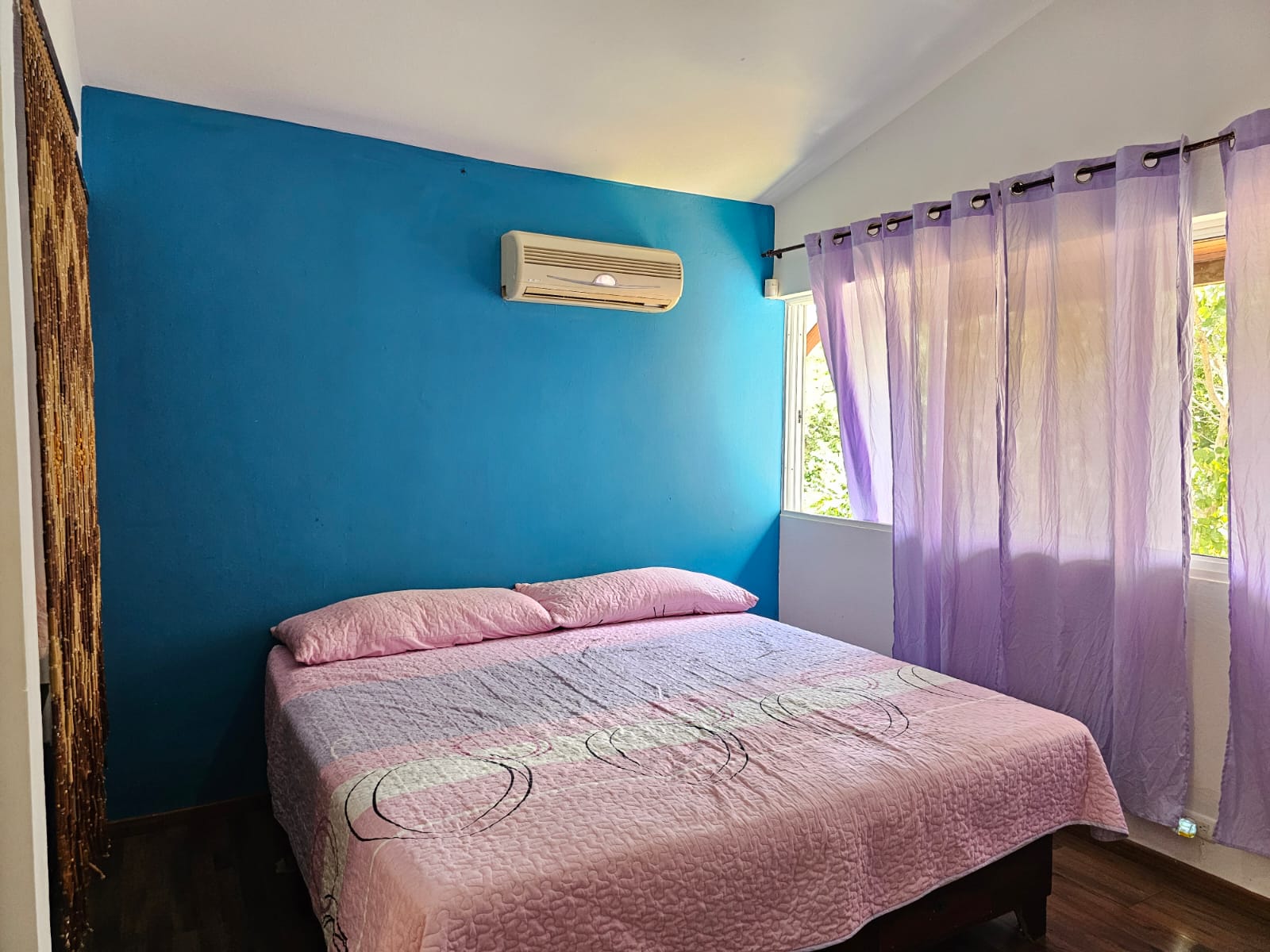 buyDRproperty Bedroom with blue accent wall, pink bedding, and purple curtains in a unique Sosua villa. Sosua Real Estate