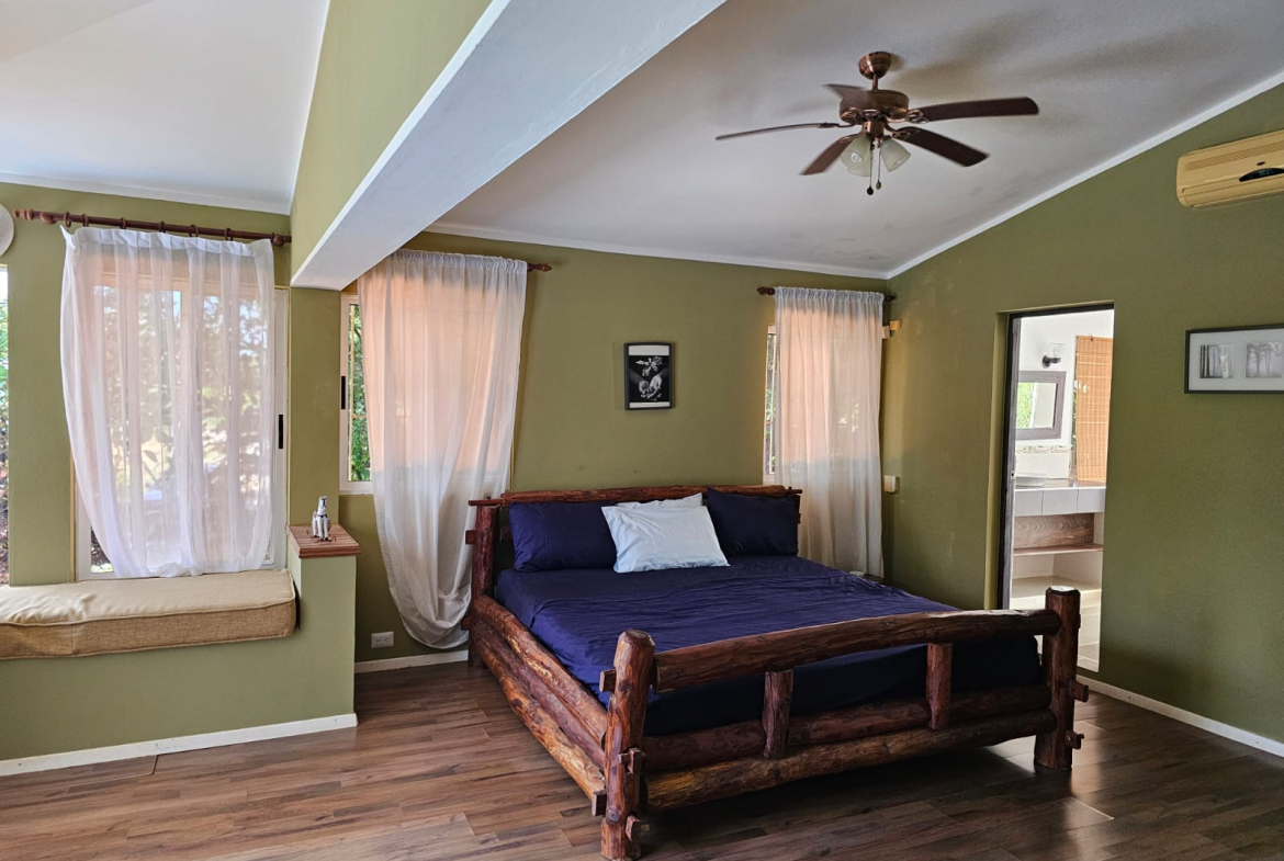buyDRproperty Bedroom in a unique Sosua villa with a log bed, light curtains, and ensuite bathroom. Sosua Real Estate