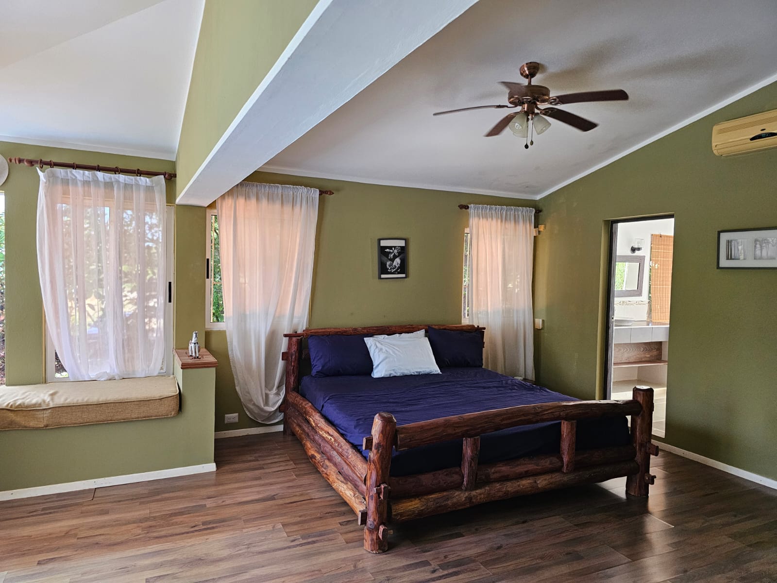 buyDRproperty Bedroom in a unique Sosua villa with a log bed, light curtains, and ensuite bathroom. Sosua Real Estate