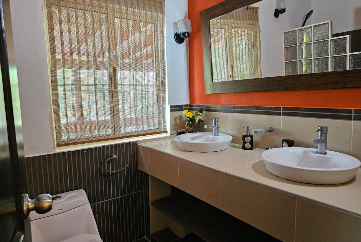 buyDRproperty Bathroom with double sinks, toilet, and window with blinds in a unique Sosua villa. Sosua Real Estate