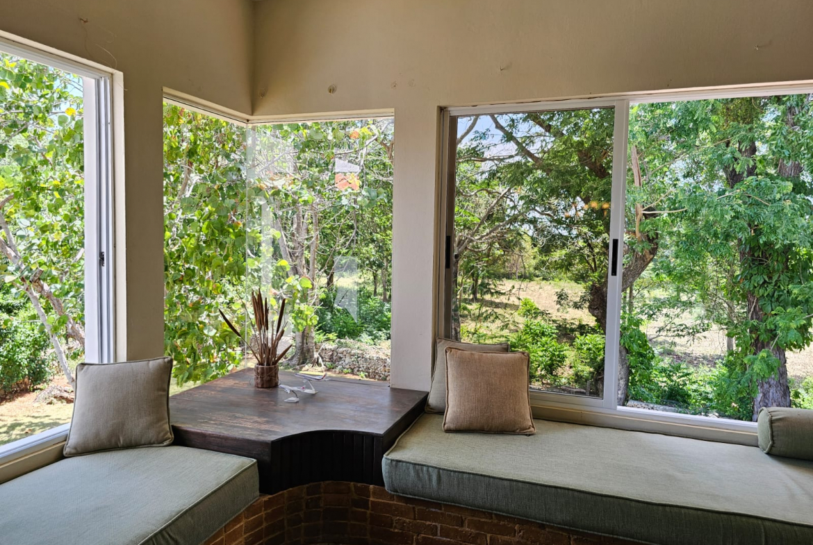 buyDRproperty Unique villa reading nook with garden view. Cushions and window seats create a cozy space. Sosua Real Estate