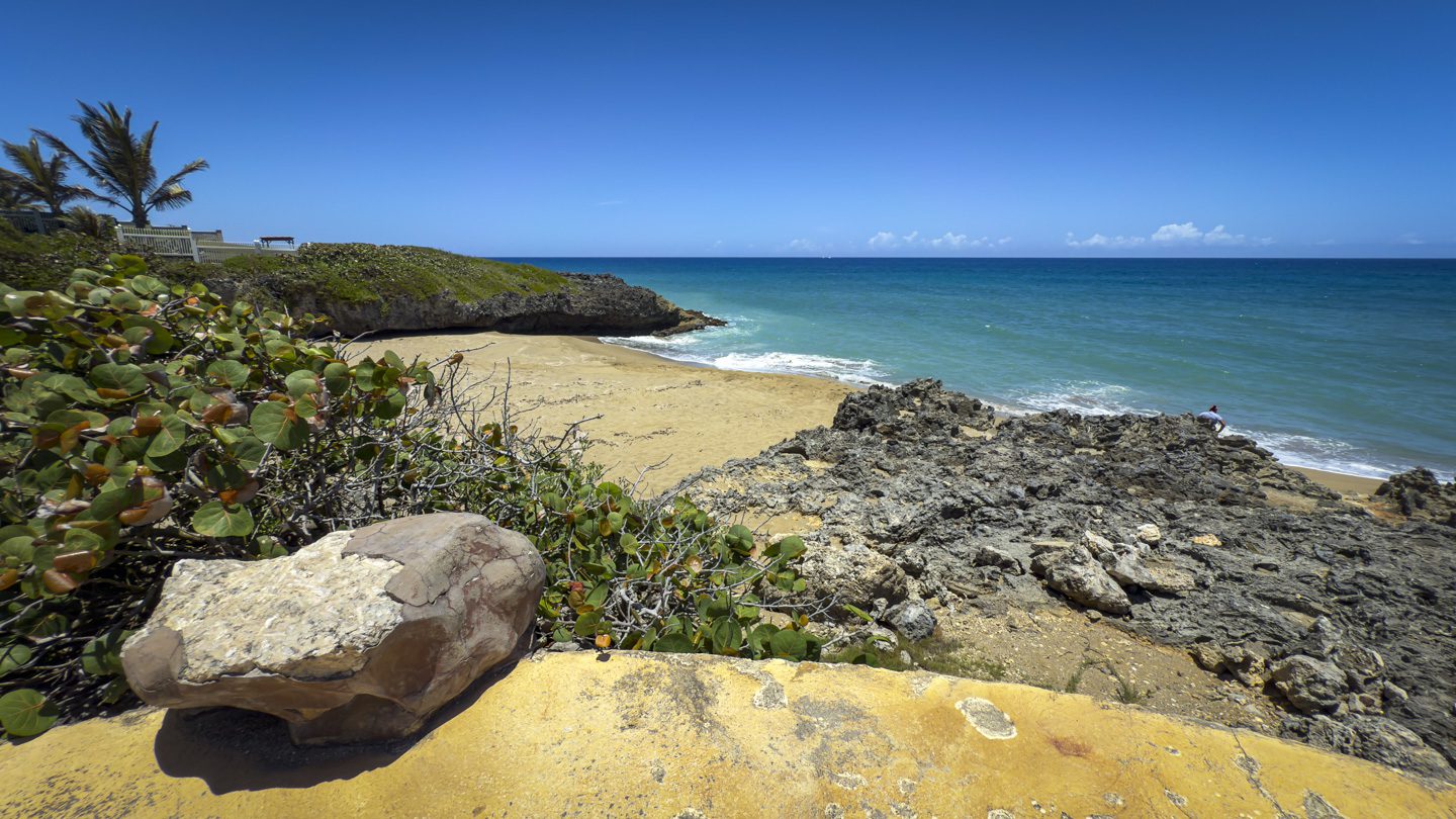 buyDRproperty Scenic coastal view with beach, rocks, and turquoise ocean under a clear blue sky. Sosua Real Estate