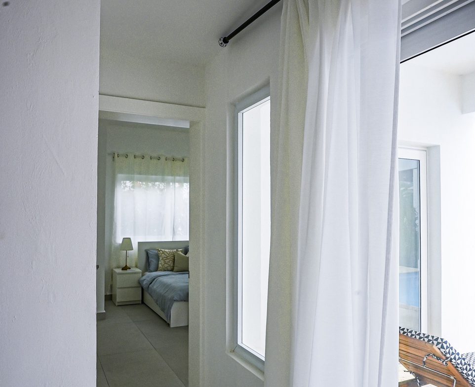 buyDRproperty Modern bedroom interior with sheer white curtains and a view of a lounge chair Sosua Real Estate
