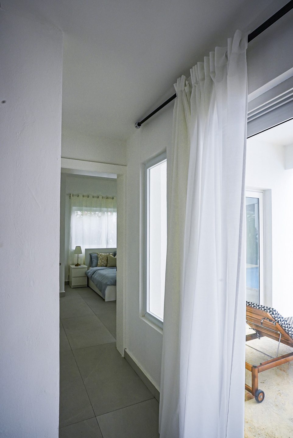 buyDRproperty Modern bedroom interior with sheer white curtains and a view of a lounge chair Sosua Real Estate