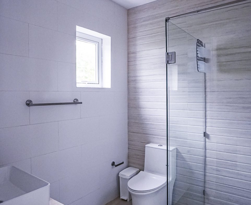 buyDRproperty Modern bathroom with white tile, glass shower, and toilet. Sosua Real Estate