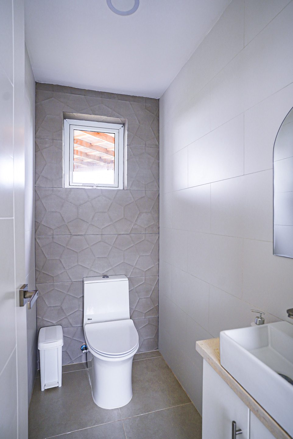 buyDRproperty Modern powder room with geometric tile accent wall, toilet, and small window. Sosua Real Estate