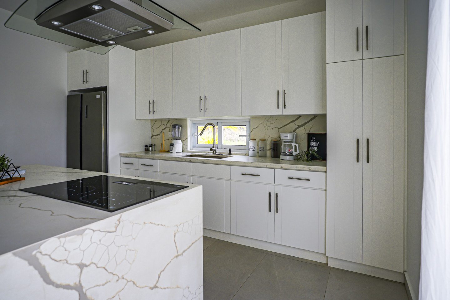 buyDRproperty Modern kitchen with white cabinets, marble countertops, and a black stovetop. Sosua Real Estate