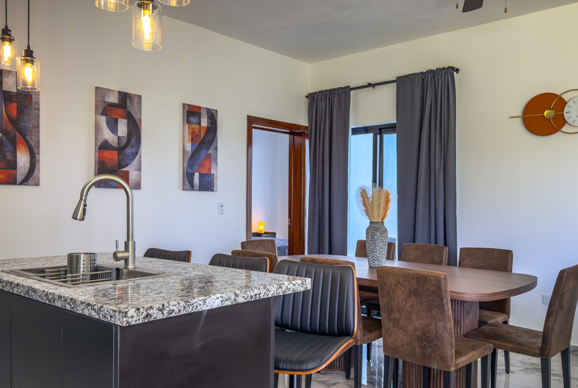 buyDRproperty Modern kitchen and dining area in a Sosua Ocean Village villa, featuring a kitchen island, dining table, and decorative artwork. Sosua Real Estate