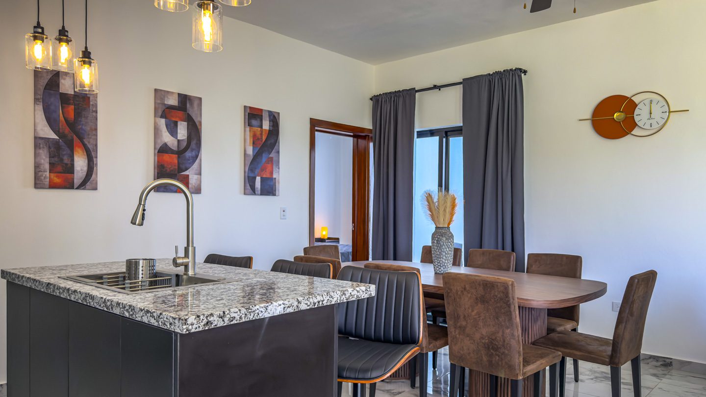 buyDRproperty Modern kitchen and dining area in a Sosua Ocean Village villa, featuring a kitchen island, dining table, and decorative artwork. Sosua Real Estate