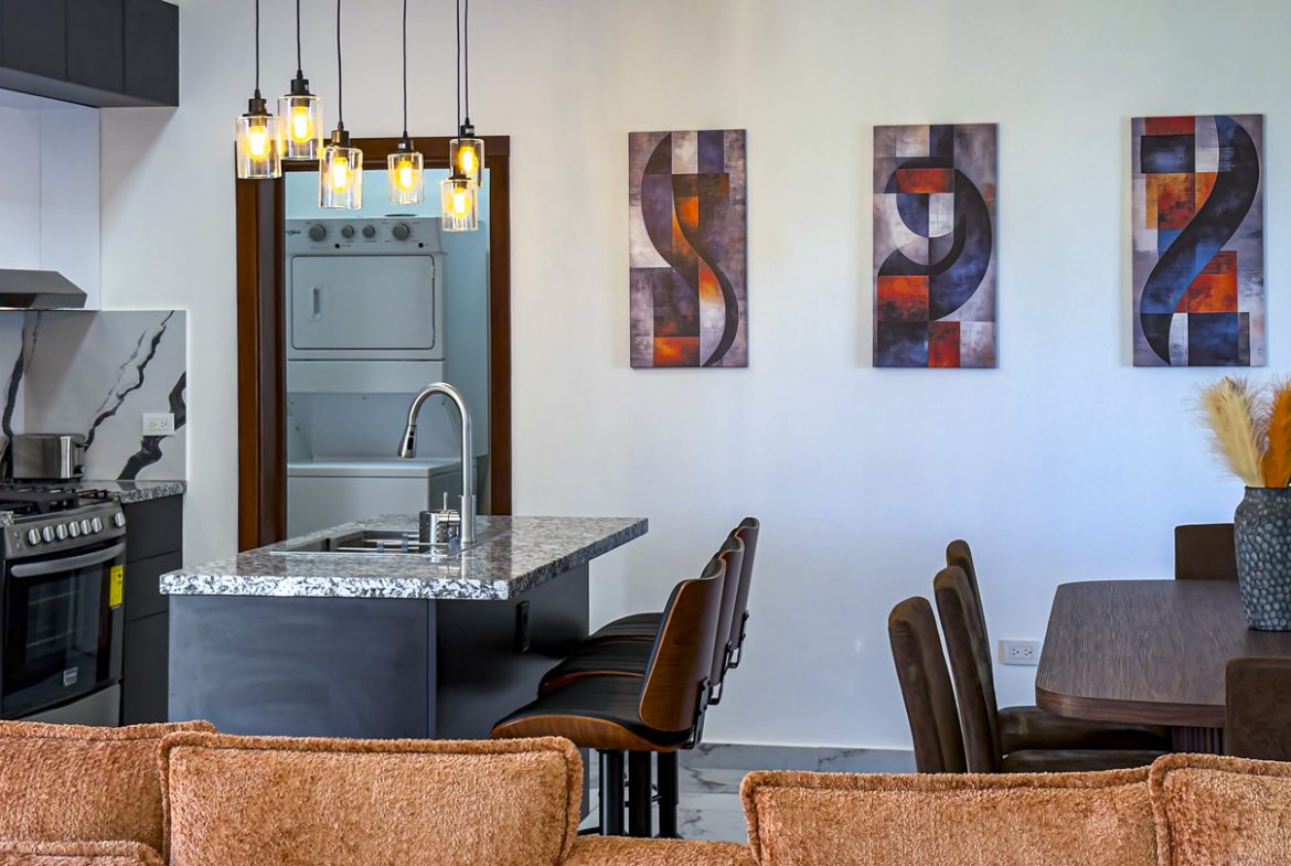 buyDRproperty Modern kitchen and dining area in a Sosua Ocean Village villa with island, artwork, and hanging lights. Sosua Real Estate