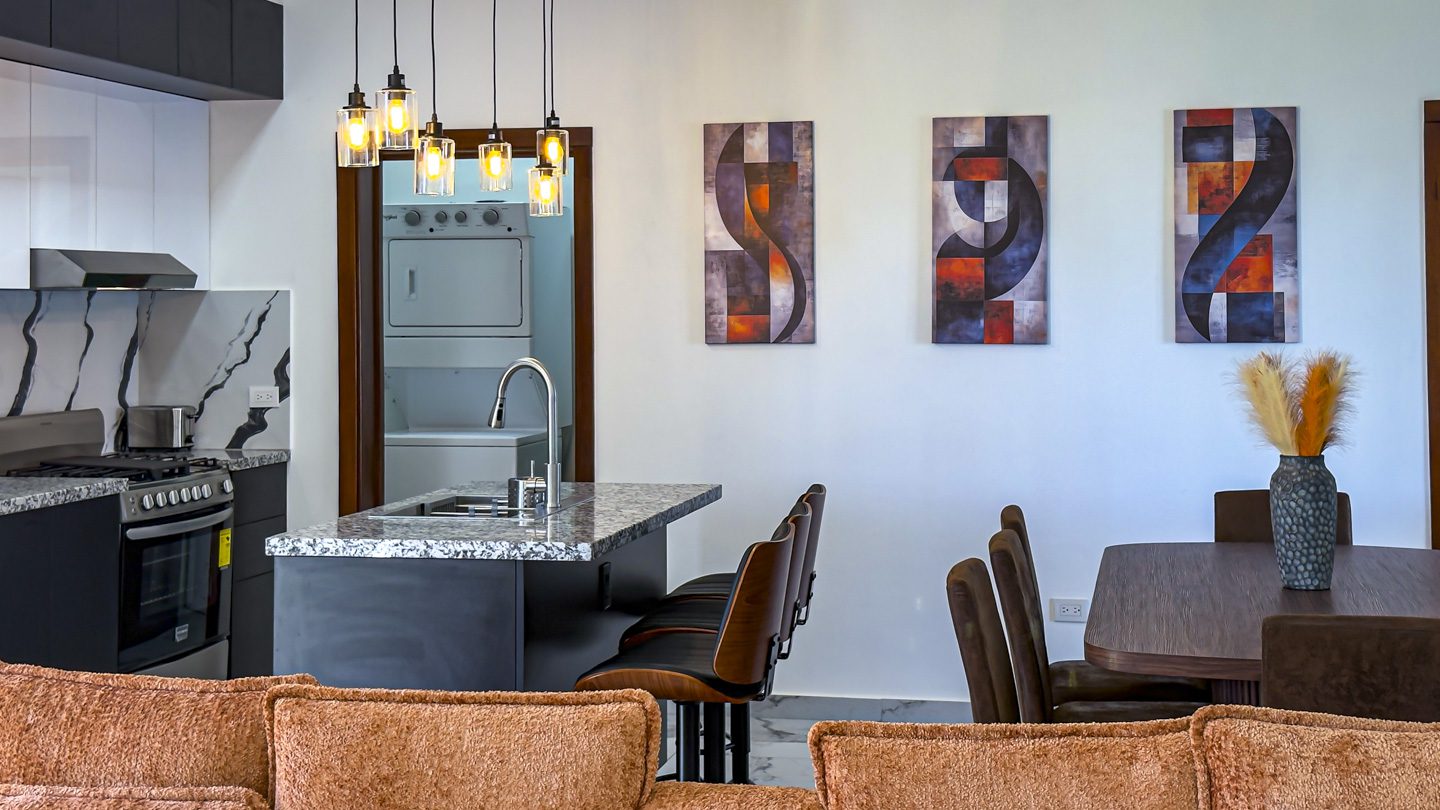 buyDRproperty Modern kitchen and dining area in a Sosua Ocean Village villa with island, artwork, and hanging lights. Sosua Real Estate