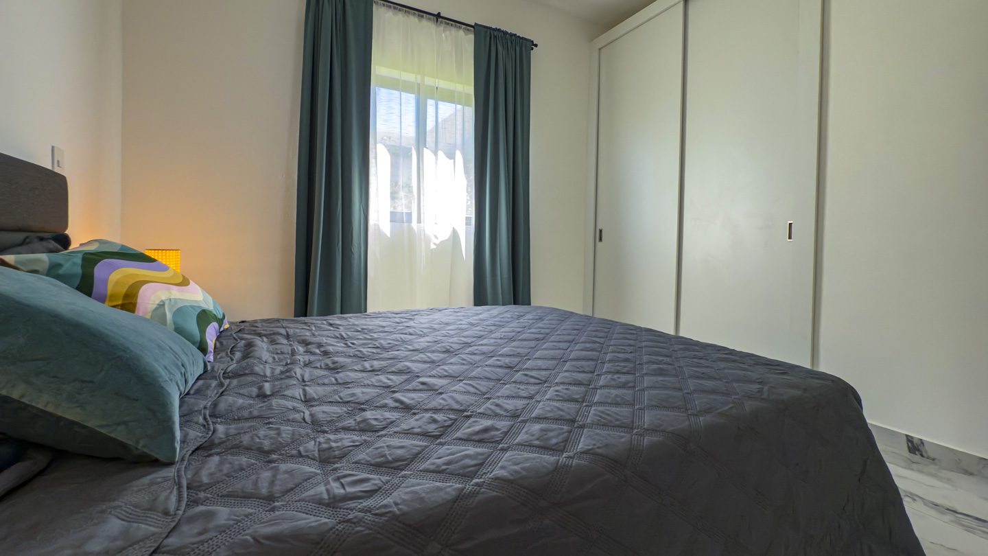 buyDRproperty Modern bedroom in a 3BR Villa Sosua Ocean Village with gray quilt and curtains. Sosua Real Estate