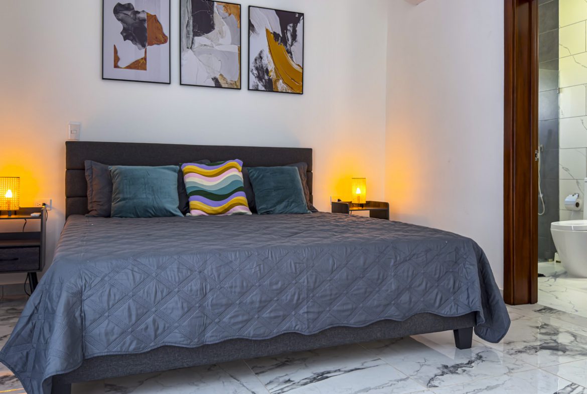 buyDRproperty Modern bedroom in a villa with a bed, nightstands, and bathroom access. Sosua Real Estate