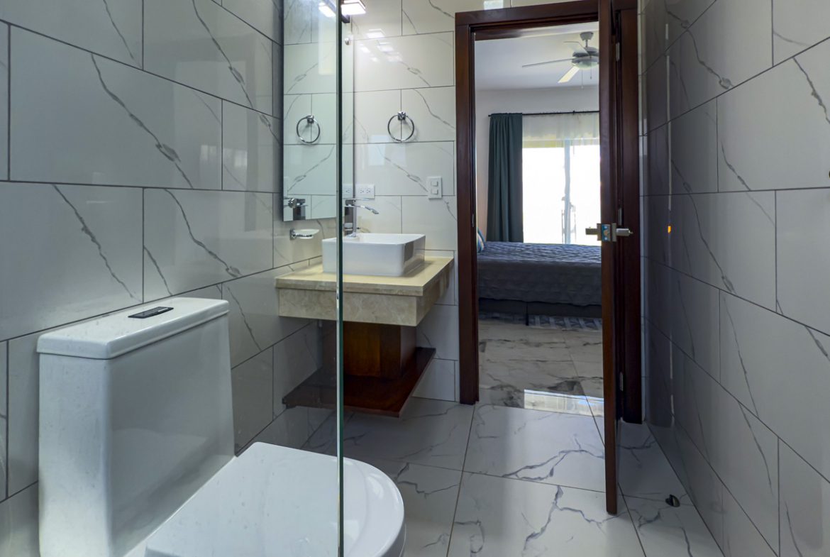 buyDRproperty Modern bathroom with marble tile, sink, and doorway to bedroom in a Sosua Ocean Village villa. Sosua Real Estate