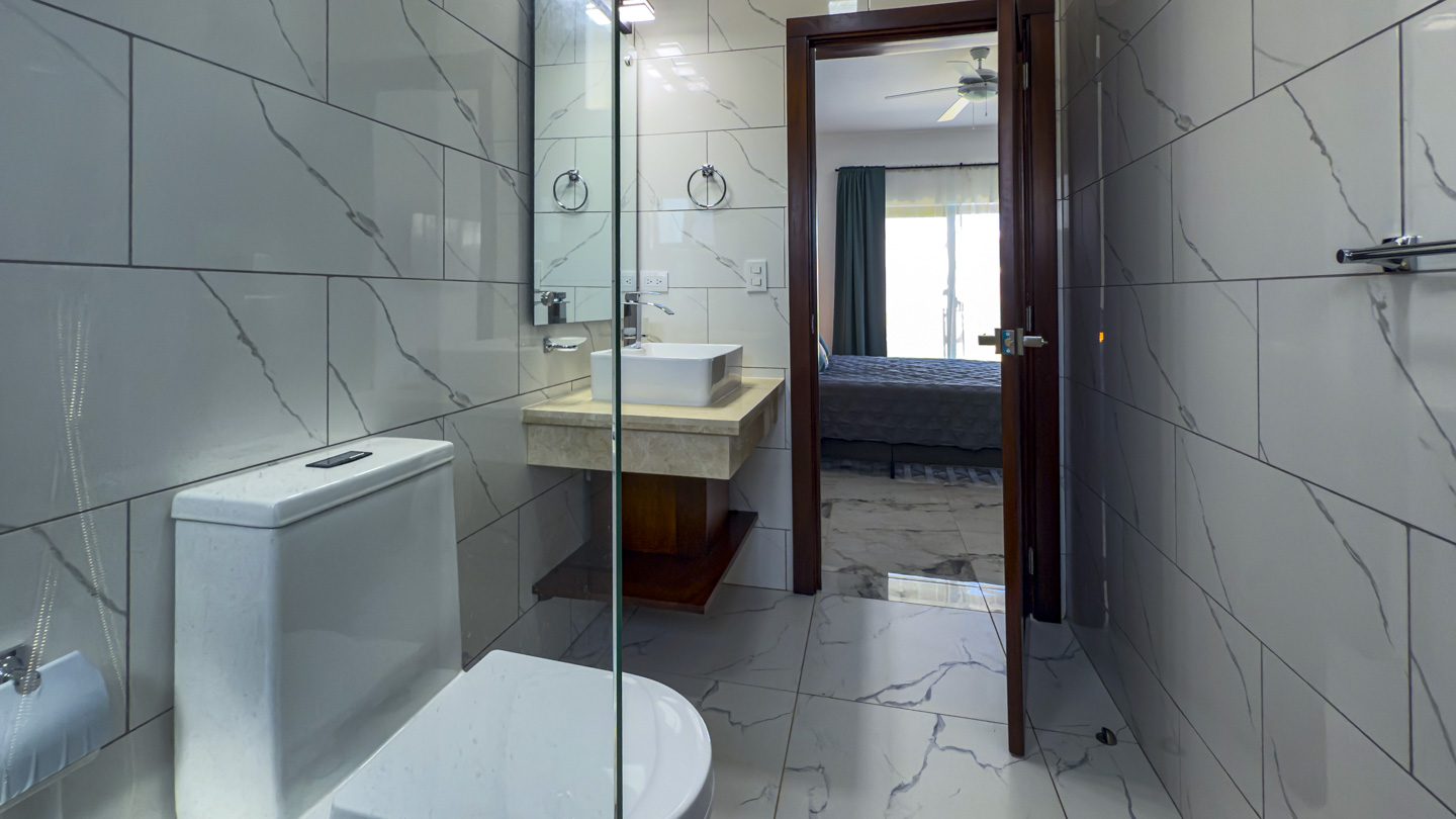 buyDRproperty Modern bathroom with marble tile, sink, and doorway to bedroom in a Sosua Ocean Village villa. Sosua Real Estate