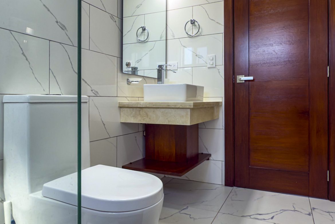 buyDRproperty Modern bathroom with white marble tiles, floating vanity, and dark wood door Sosua Real Estate