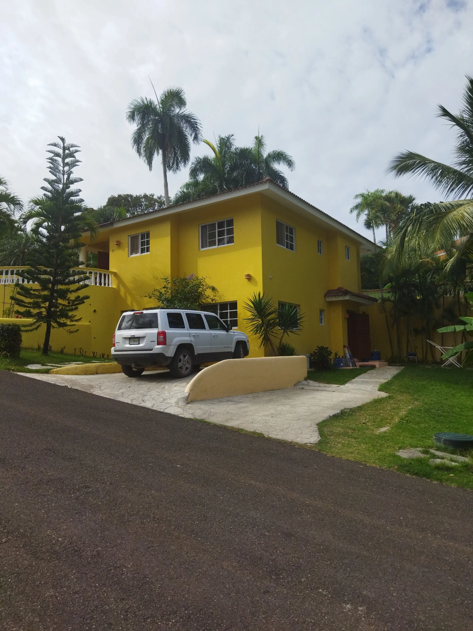 buyDRproperty Charming yellow villa with white Jeep parked in the driveway. Lush landscaping. Sosua Real Estate
