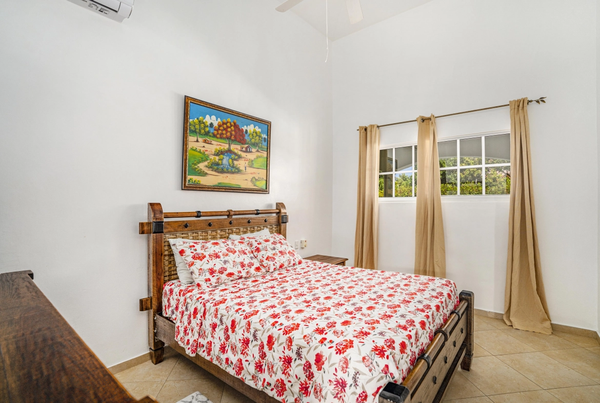 buyDRproperty Bedroom with a wooden bed frame and oversized floral bedding. A painting hangs on the wall. Sosua Real Estate