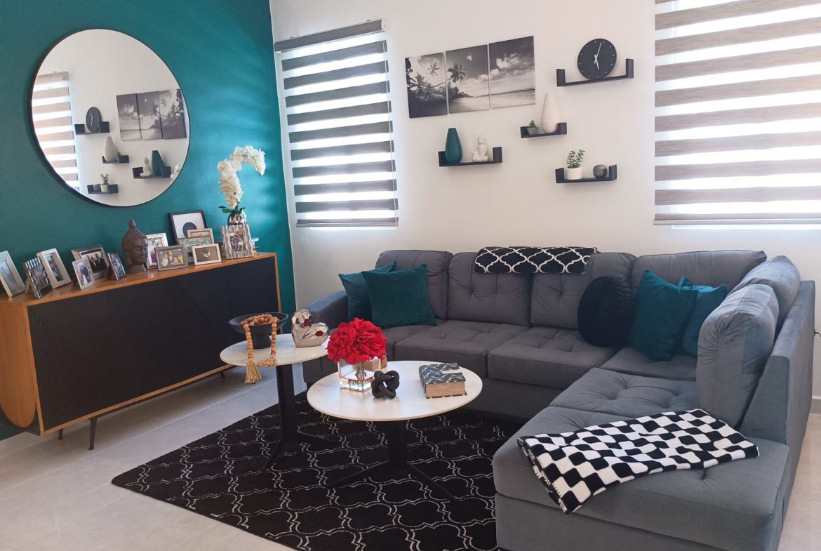 buyDRproperty Modern living room with gray sectional sofa, black rug, and teal accent wall. Sosua Real Estate