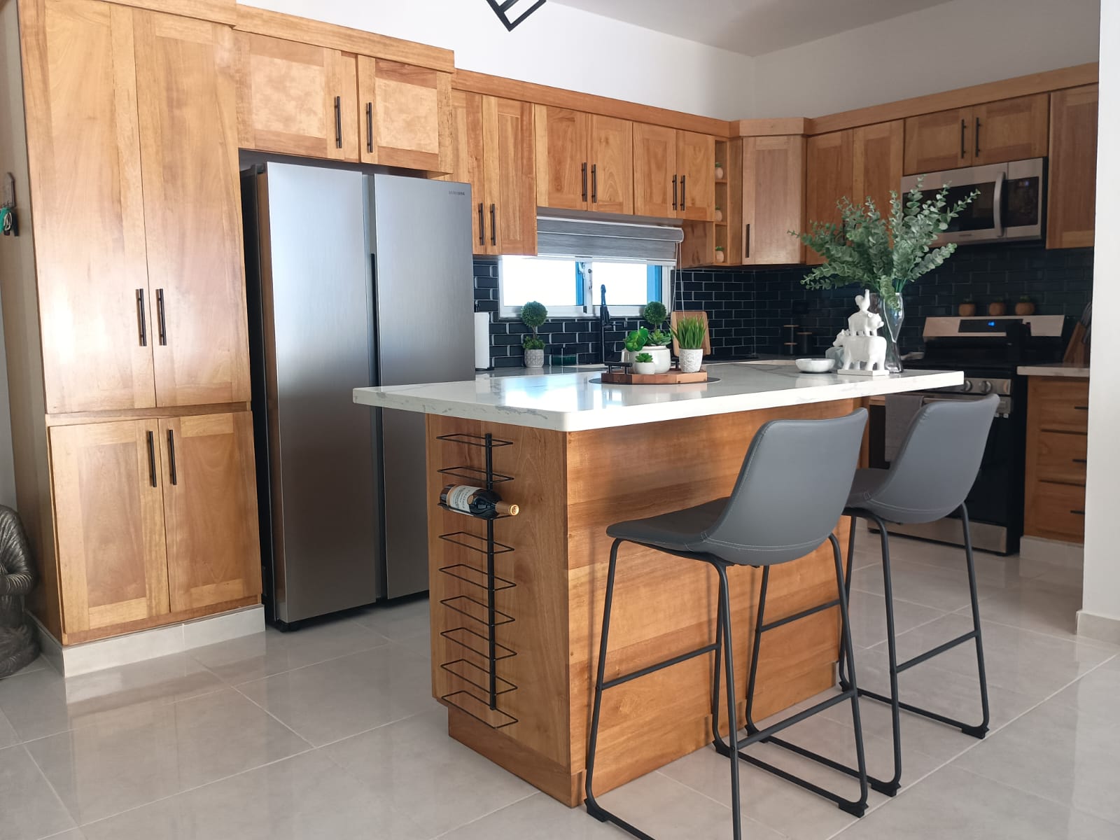 buyDRproperty Modern kitchen with wooden cabinets and island, featuring bar stools and wine rack. Sosua Real Estate