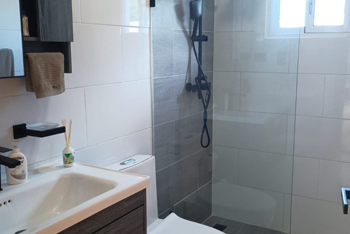buyDRproperty Modern bathroom with gray and white tiles, glass shower and black fixtures. Sosua Real Estate
