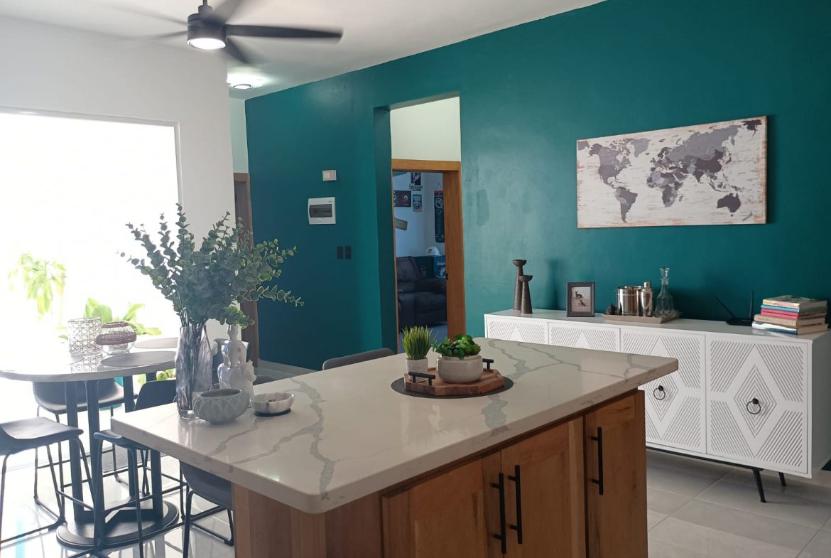 buyDRproperty Modern kitchen interior with teal accent wall, island, and white cabinets. Sosua Real Estate
