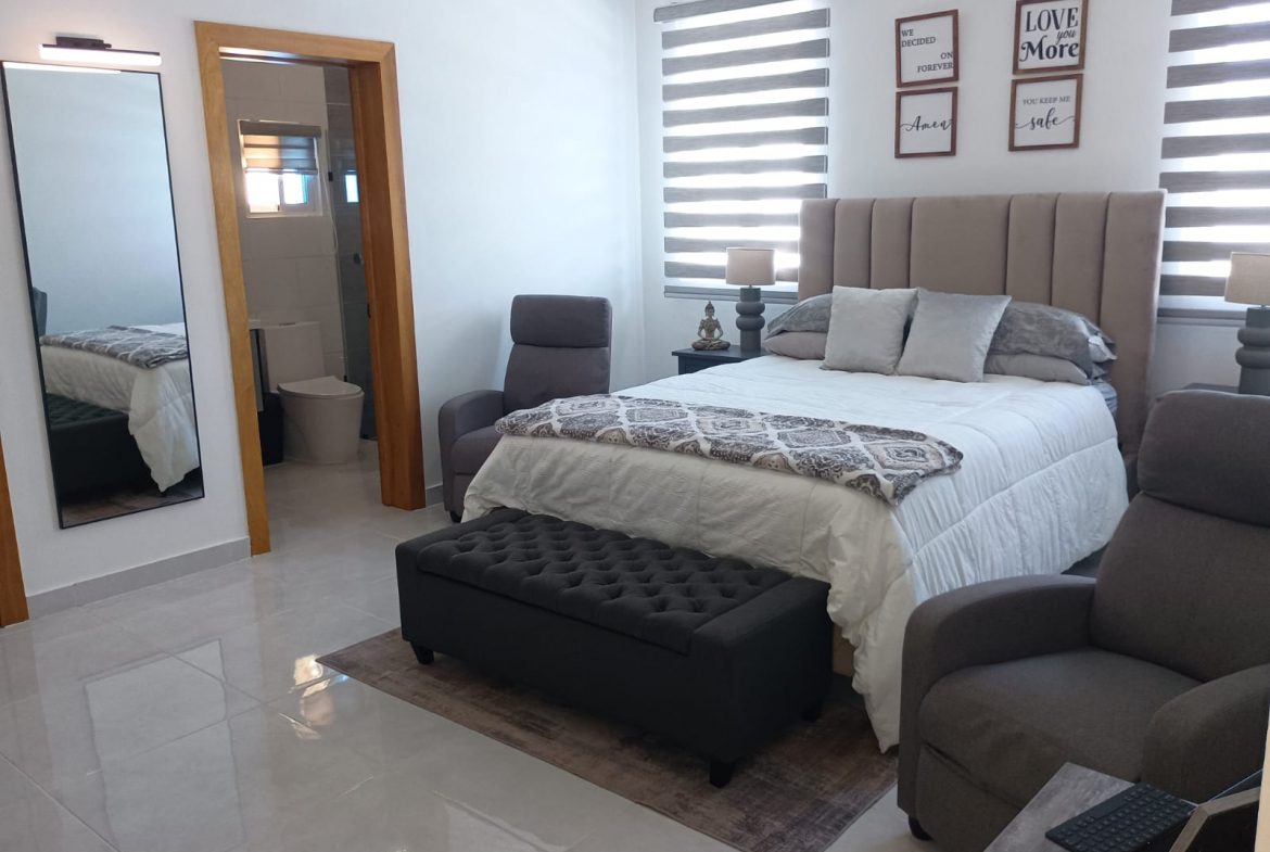 buyDRproperty Modern bedroom with neutral tones, bed, and two armchairs. Sosua Real Estate