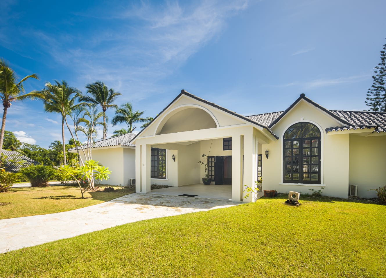 buyDRproperty White tropical home with arched doorway and lush green lawn, perfect for vacation rentals. Sosua Real Estate