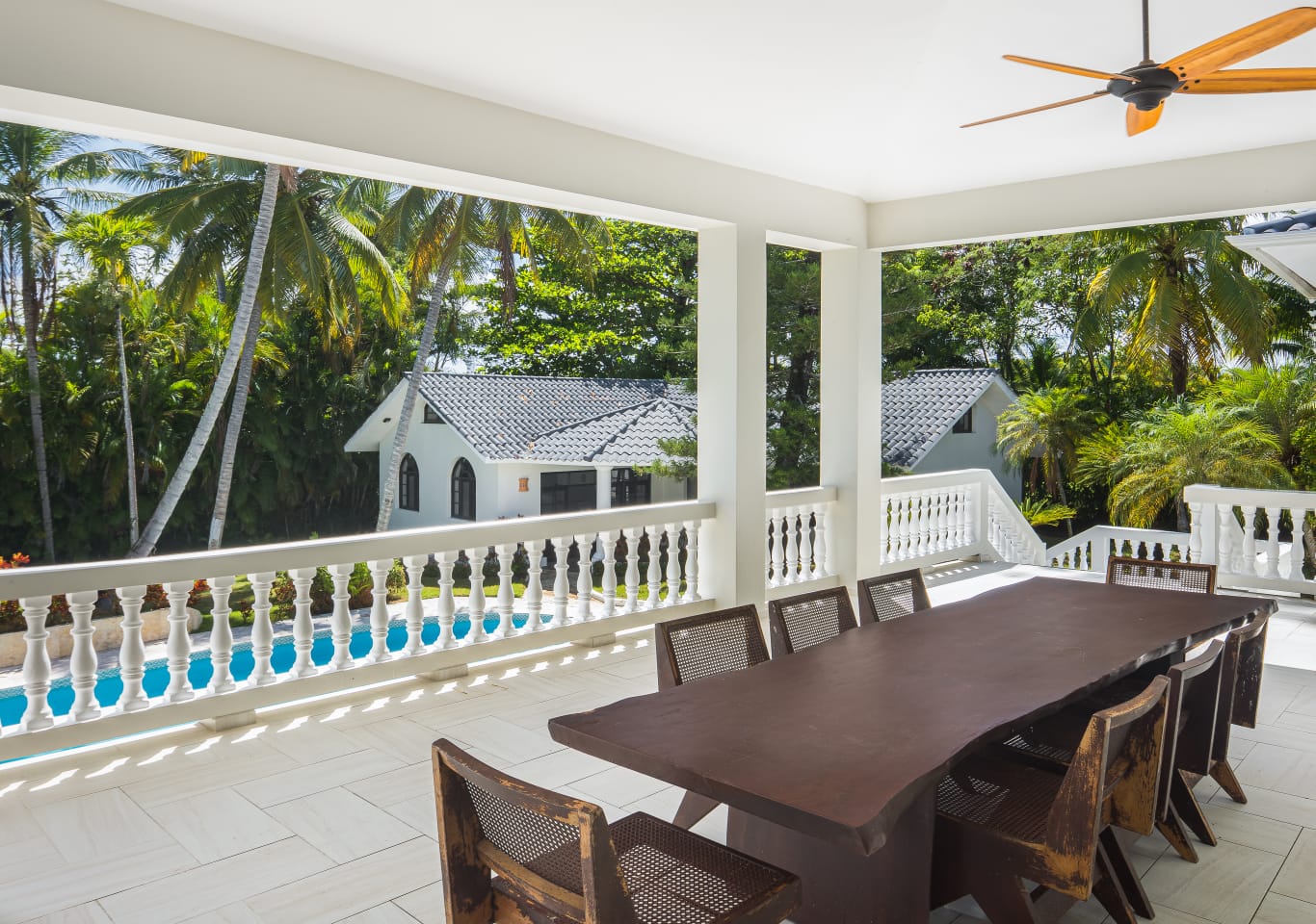 buyDRproperty Luxury outdoor dining area with wooden table and chairs, overlooking pool and tropical view. Sosua Real Estate