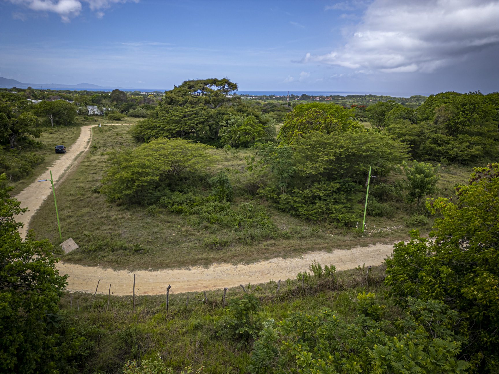buyDRproperty Dirt road winding through lush Caribbean landscape with ocean view. Sosua Real Estate