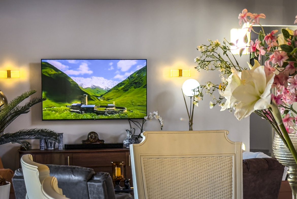 buyDRproperty Living room with TV showing a mountain landscape, decorative plants, and stylish furniture. Sosua Real Estate
