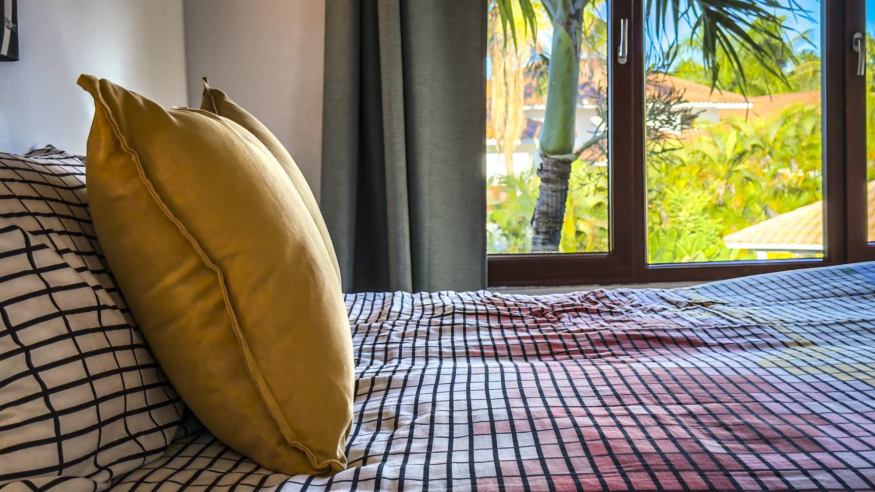 buyDRproperty Bedroom in a luxury villa with ocean views, featuring a bed with patterned linens and a window overlooking tropical foliage. Sosua Real Estate