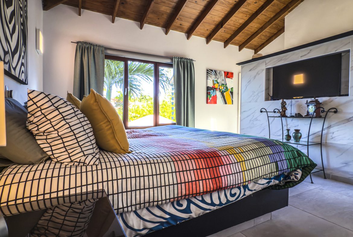 buyDRproperty Bedroom interior with ocean view villa for sale, featuring colorful bedspread, artwork, and built-in TV. Sosua Real Estate