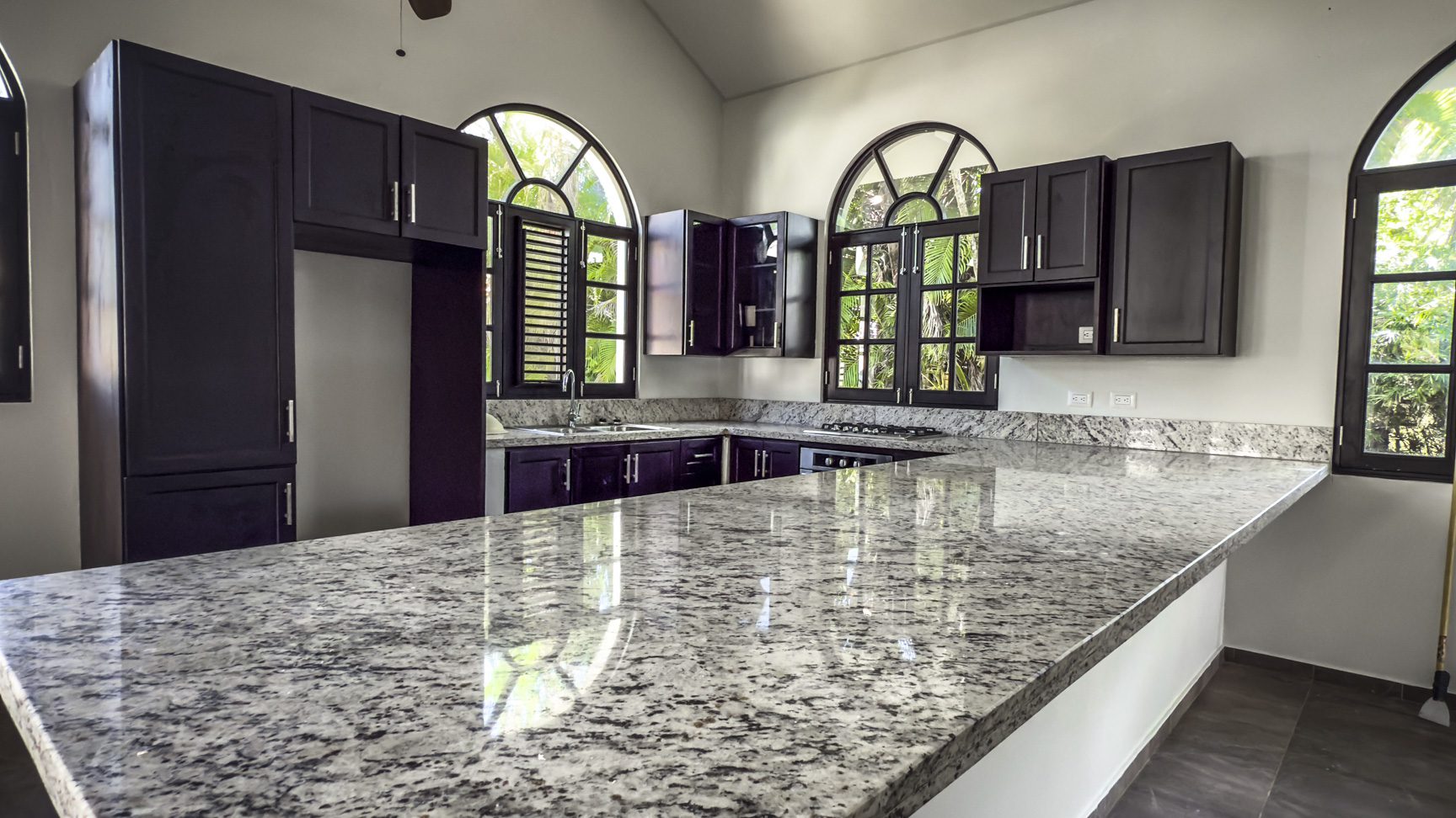 buyDRproperty Modern kitchen with dark cabinets, granite countertops, and arched windows Sosua Real Estate