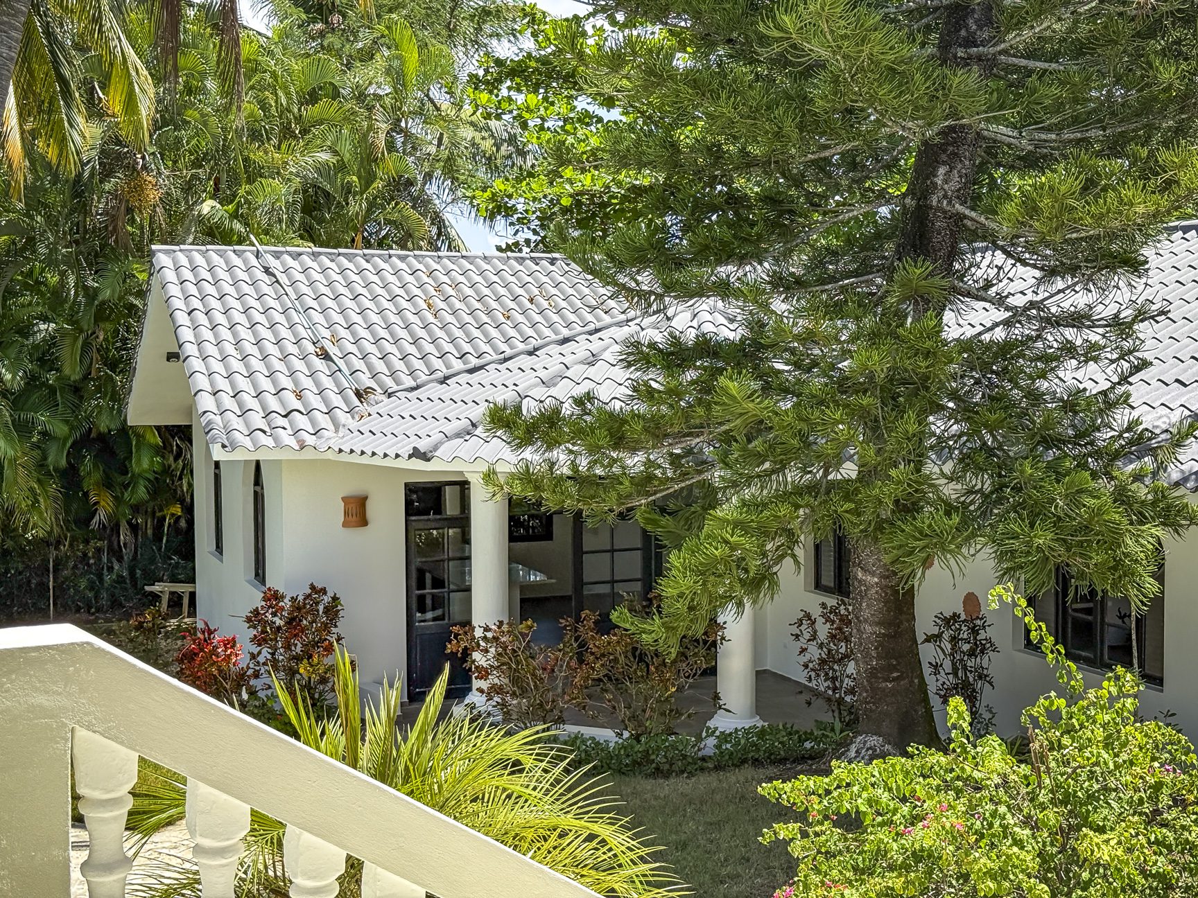 buyDRproperty White stucco vacation home with gray tile roof surrounded by lush tropical greenery. Sosua Real Estate