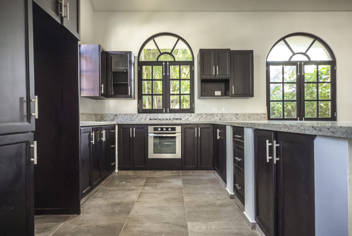 buyDRproperty Modern kitchen with dark cabinets, granite countertops, and arched windows. Sosua Real Estate