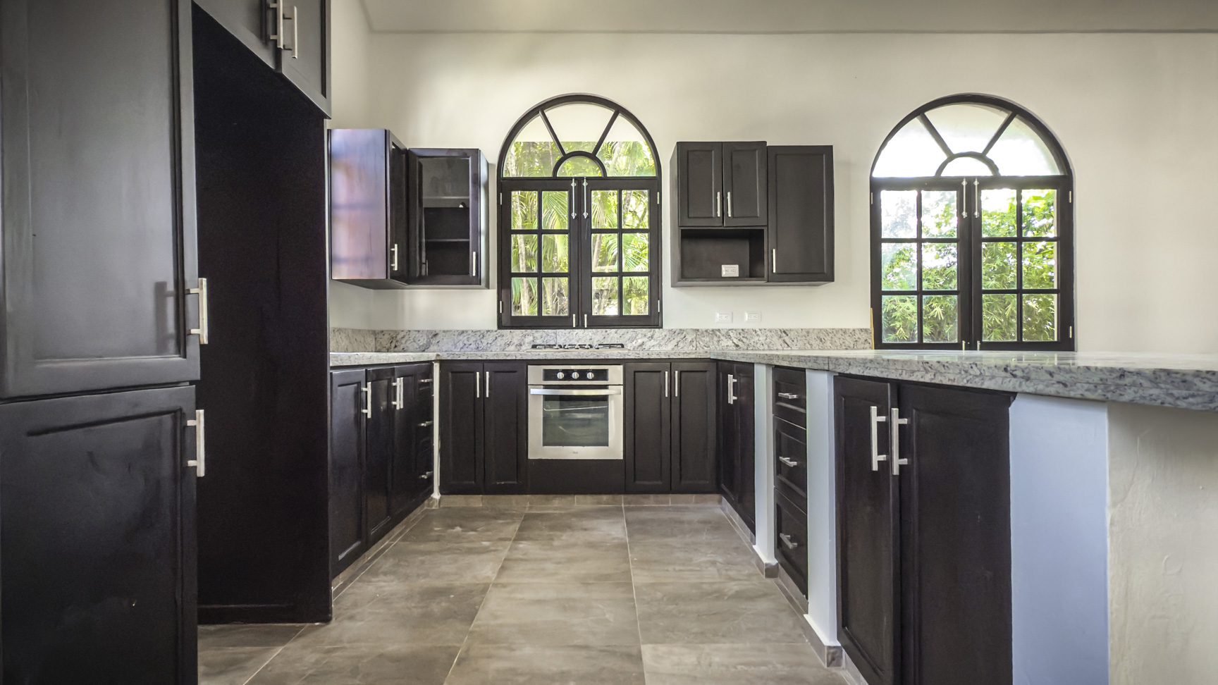 buyDRproperty Modern kitchen with dark cabinets, granite countertops, and arched windows. Sosua Real Estate