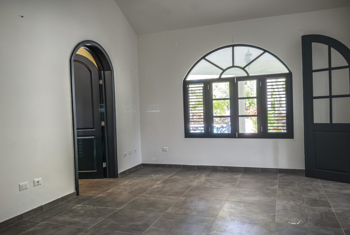 buyDRproperty Empty room with black arch doorways, black doors, and a large arched window; modern interior design. Sosua Real Estate