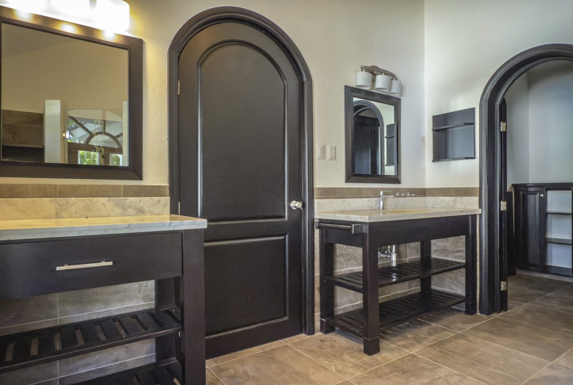 buyDRproperty Modern bathroom with dark wood vanities, arched doorways, and marble countertops. Bathroom remodel inspiration. Sosua Real Estate