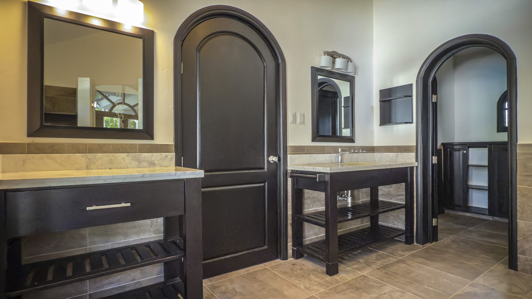 buyDRproperty Modern bathroom with dark wood vanities, arched doorways, and marble countertops. Bathroom remodel inspiration. Sosua Real Estate